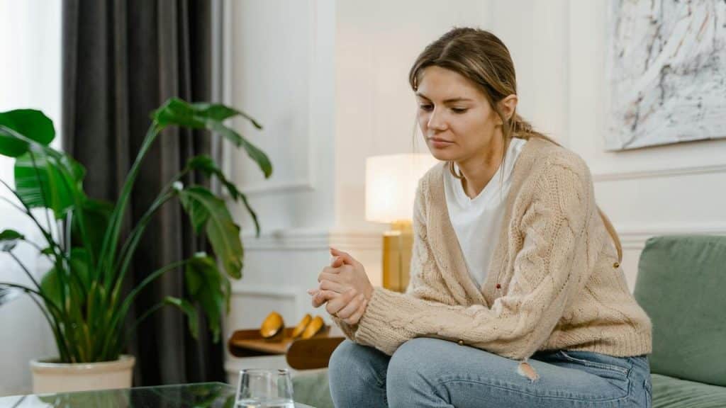 A woman sitting on a couch with a sad and thoughtful expression.