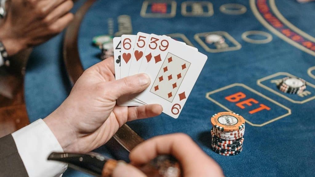 A hand holding playing cards over a casino table with chips.