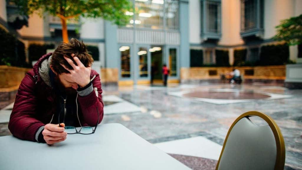 A person sitting at a table with head in hand, holding glasses.