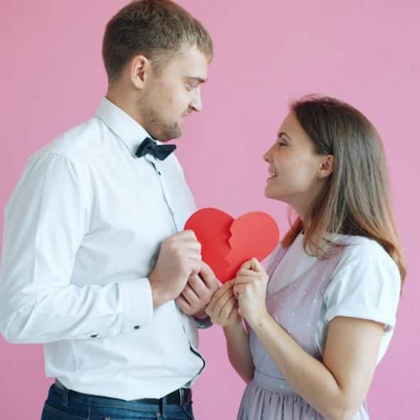 A couple holding a broken heart on a pink background.