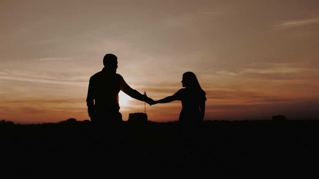 Silhouette of a couple holding hands against a sunset or sunrise.