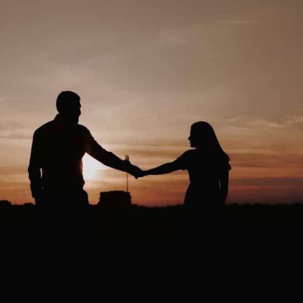 Silhouette of a couple holding hands against a sunset or sunrise.