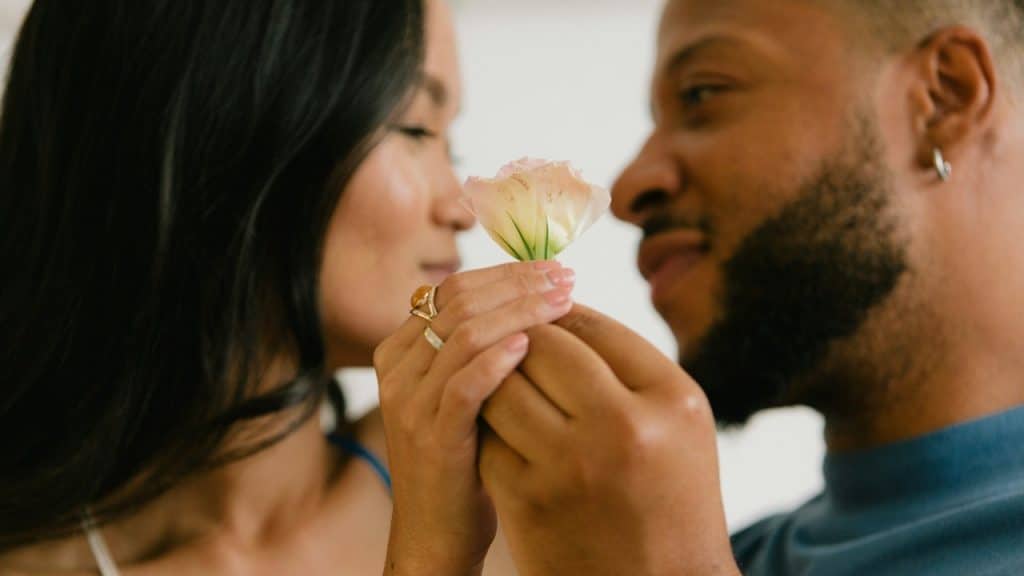 A couple holding a flower and smiling at each other.