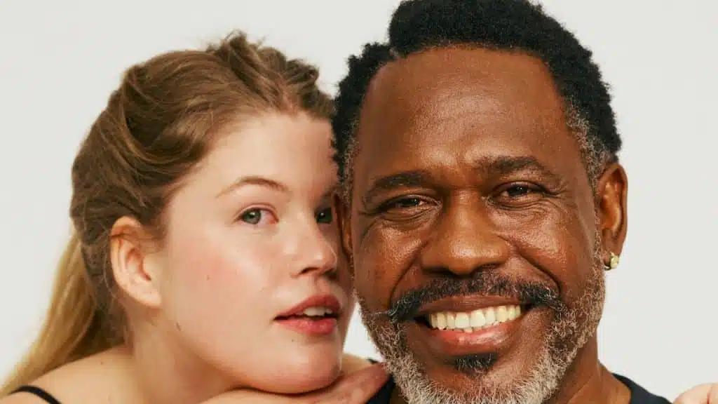 An older man smiling while a younger woman rests her head on his shoulder.