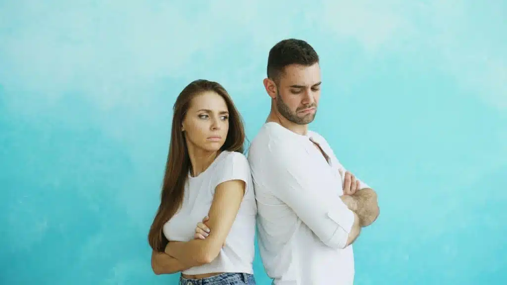 A couple standing back-to-back with arms crossed.