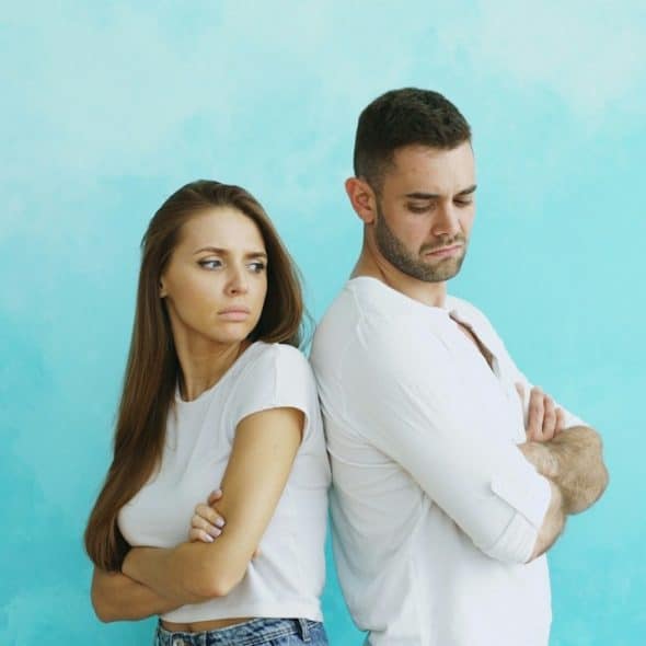 A couple standing back-to-back with arms crossed.