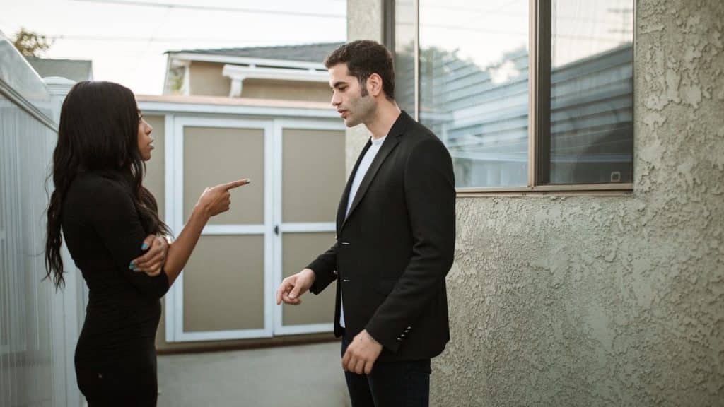 Man and woman arguing outside near a building, with the woman pointing her finger.