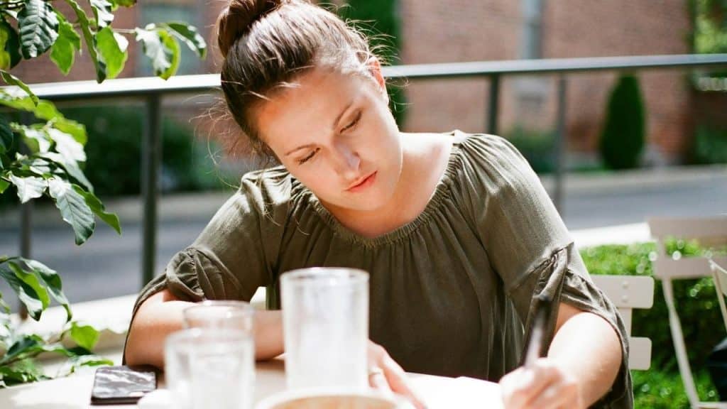 A woman writing at an outdoor table.