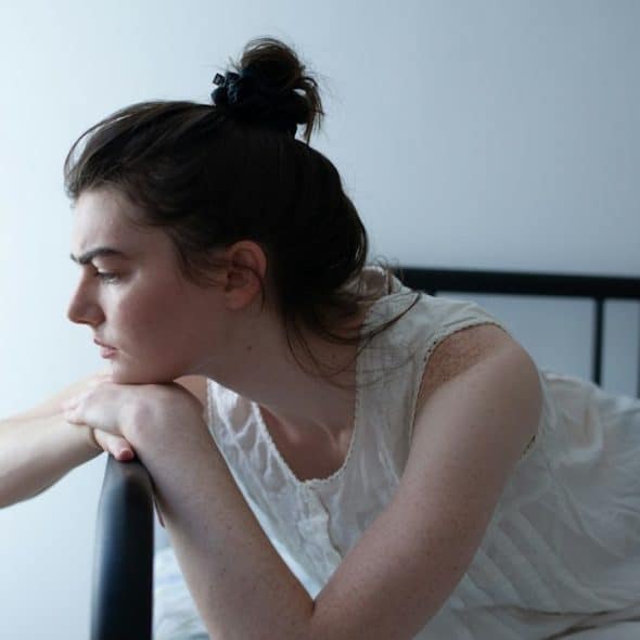A woman looking depressed and resting her face on her hands, which are placed on a couch’s arm.