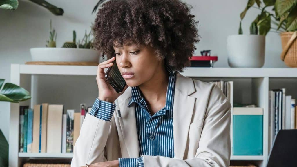 A woman sitting at a desk talking on the phone with a serious expression.