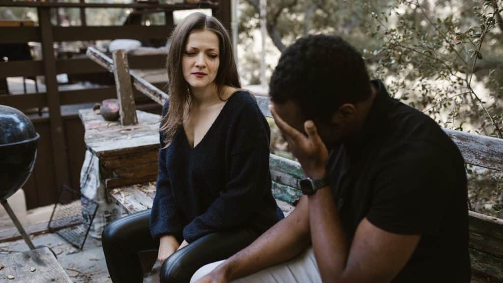 Distressed couple sitting outside on a bench.