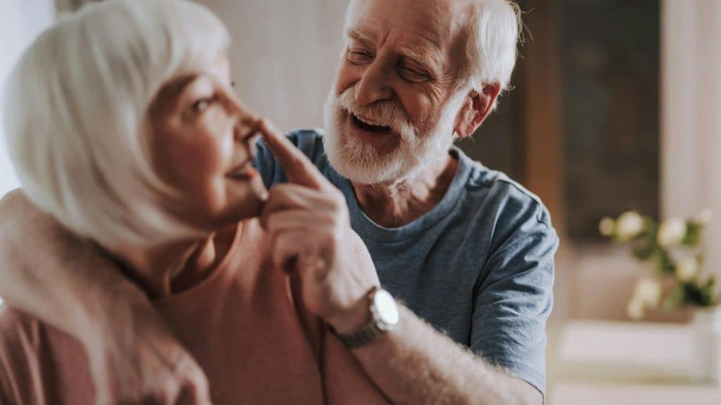 An older man smiling and playfully touching a woman's nose.