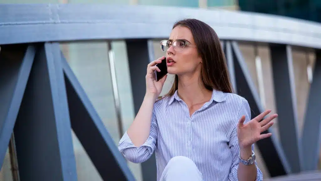 A serious woman talking on the phone while standing in the street.