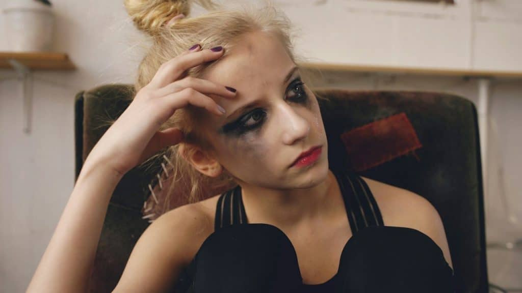 A young woman with smudged makeup sits in a chair.