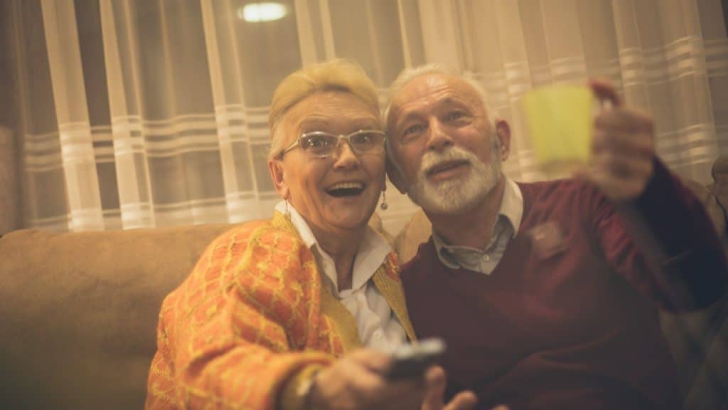 An elderly couple watching together in living room.