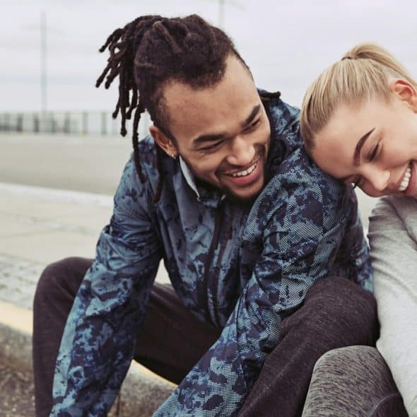 A laughing young couple sitting on a road together, taking a break from a run on an overcast day.
