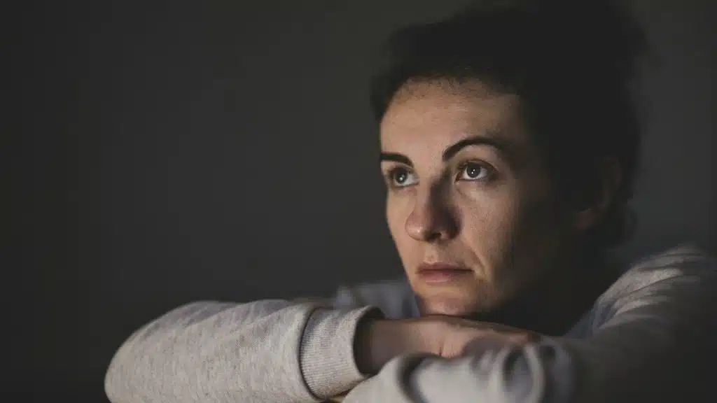 A woman rests her chin on her crossed arms, looking off into the distance with a somber and pensive expression.