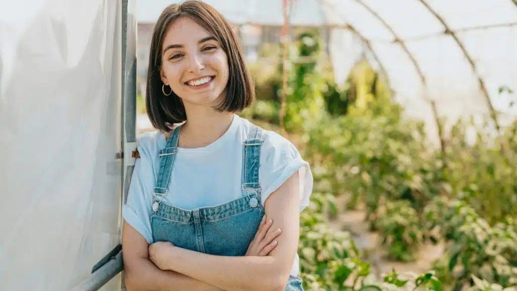 A woman standing in a greenhouse with her arms crossed.