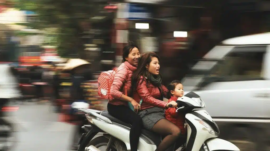 A woman driving a white motor scooter.