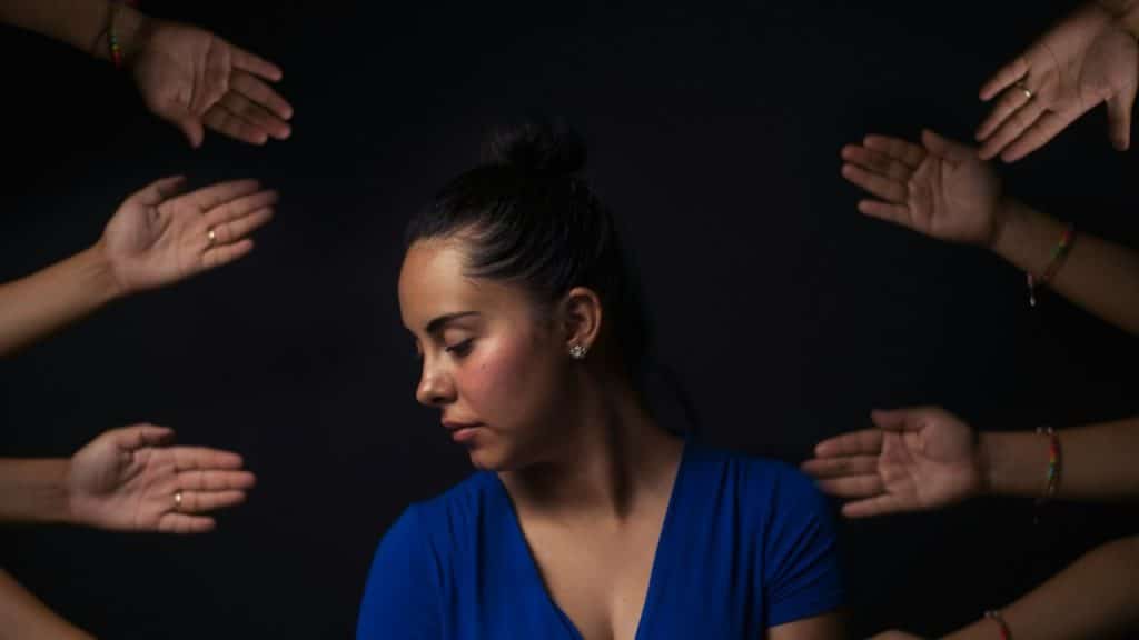 Multiple hands pointing towards a woman wearing a blue v-neck short-sleeved top.