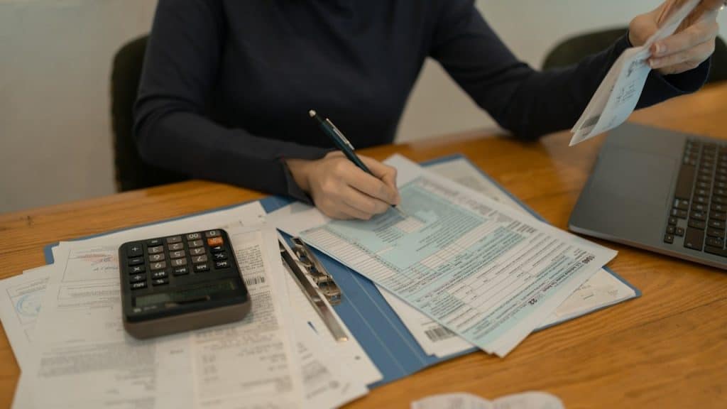 A sitting at a table with a calculator, laptop, and documents.
