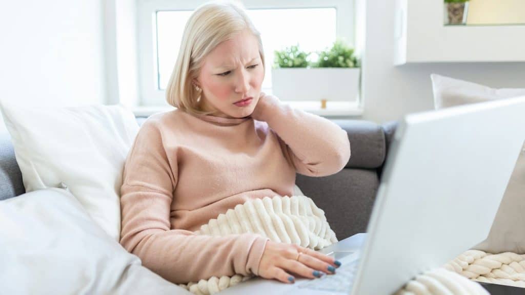 A frustrated young woman looking exhausted and massaging her neck while working on her laptop.