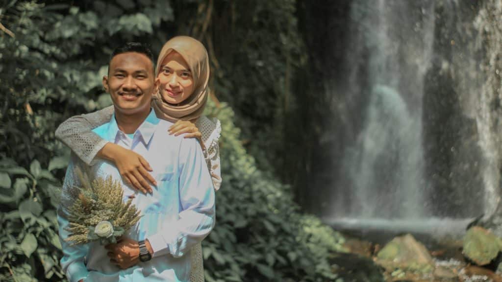 A man and woman hugging in front of a waterfall.