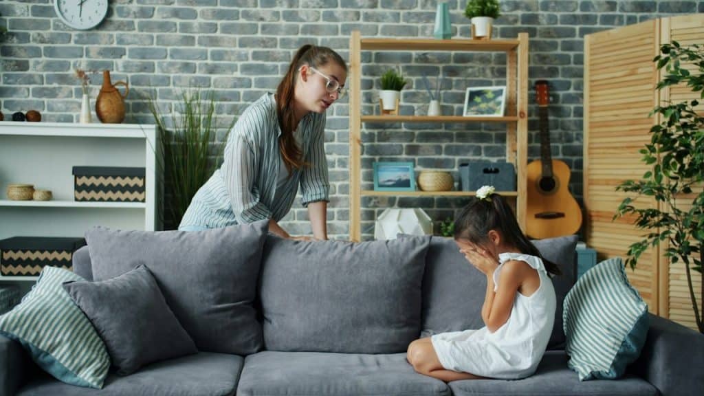 A mother scolds her crying daughter on the sofa in the living room.
