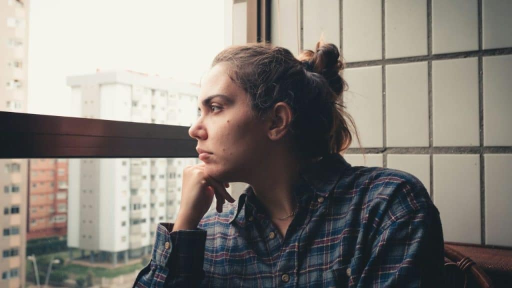 A woman in a plaid shirt rests her chin on her hand while looking out a window.