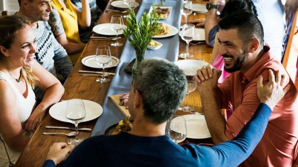 A group of people sits at a long dining table laughing together during a meal.