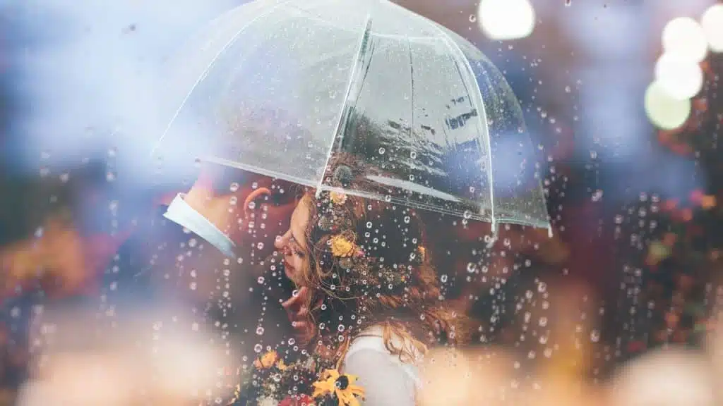 A man and a woman kissing in the rain under an umbrella.