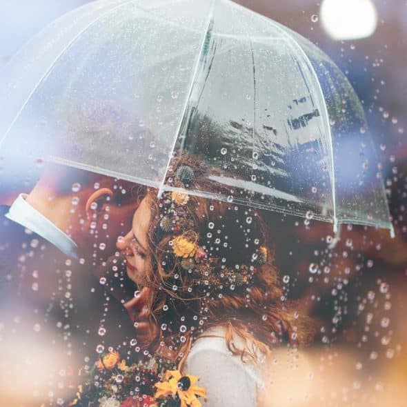 A man and a woman kissing in the rain under an umbrella.