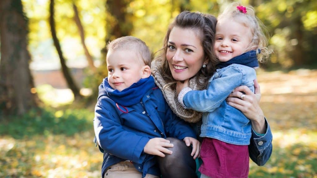 A beautiful young mother with small twins on a walk in an autumn forest.