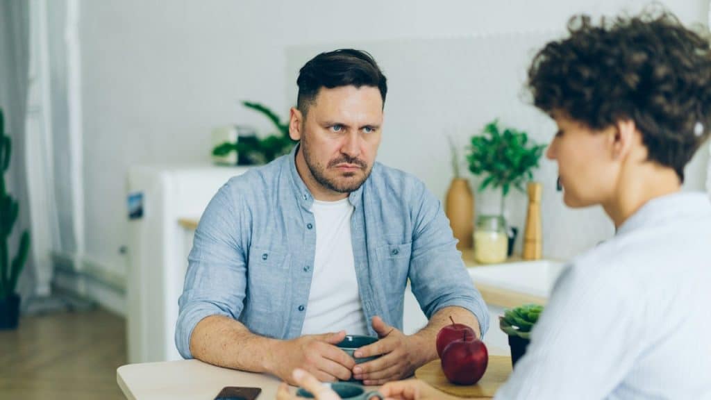 A man looking angrily at a woman while they have coffee at a table. 