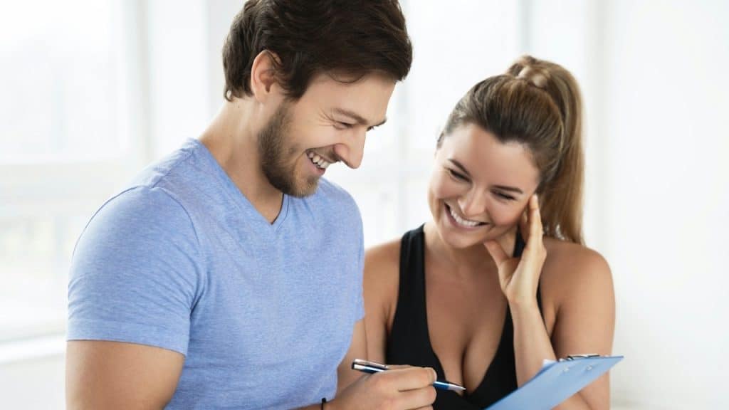 A smiling man and woman look at a blue clipboard together in a bright, white room.