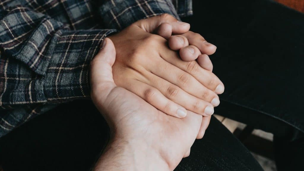 A close-up shows two people holding hands, with one person wearing a plaid shirt.