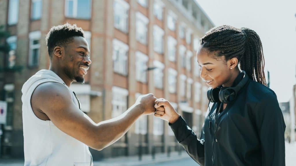 A man and woman in athletic wear share a friendly fist bump on a city street.