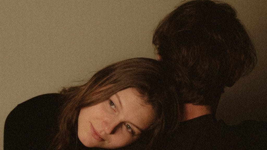 A woman rests her head on a man's shoulder in a dimly lit, intimate setting.