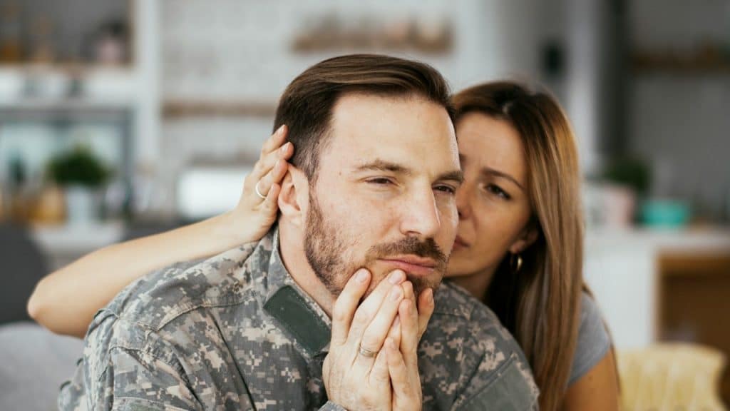 A woman gently comforting a man as he sits with a somber expression.
