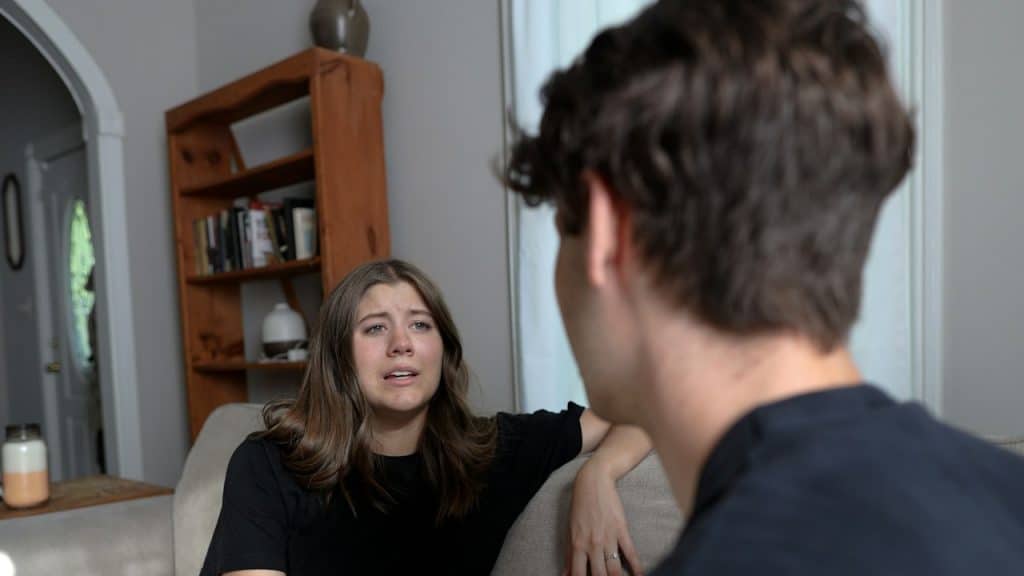 A woman sitting at a couch talking to a man.