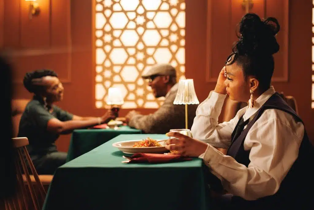 A woman sitting alone at a restaurant table is looking at a couple sitting at the other table.
