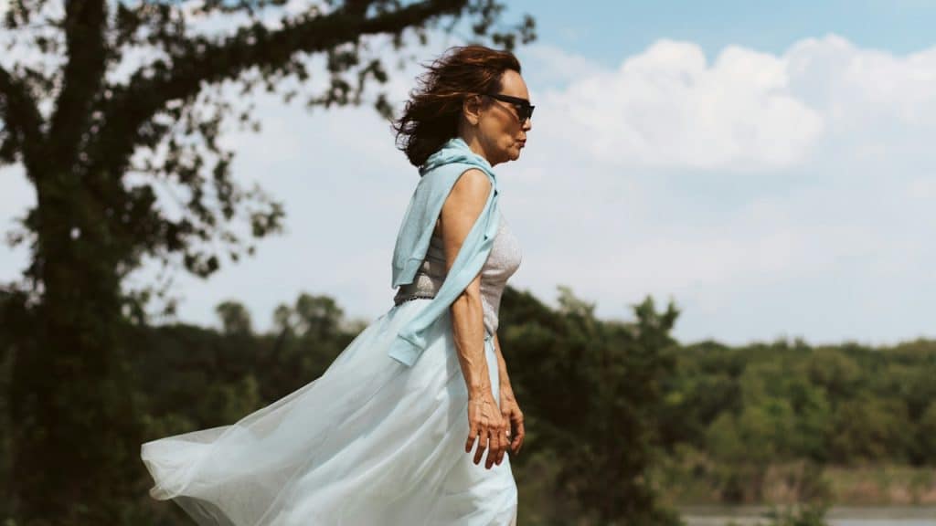 An elderly woman in a sleeveless dress and sunglasses.