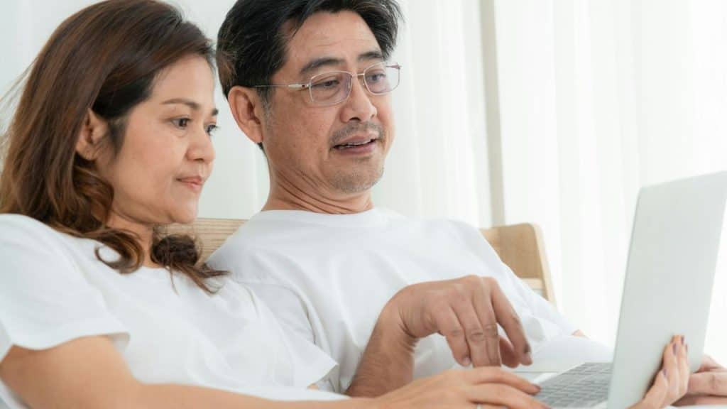 Middle-aged Asian couple in white shirts looking at a laptop together indoors.