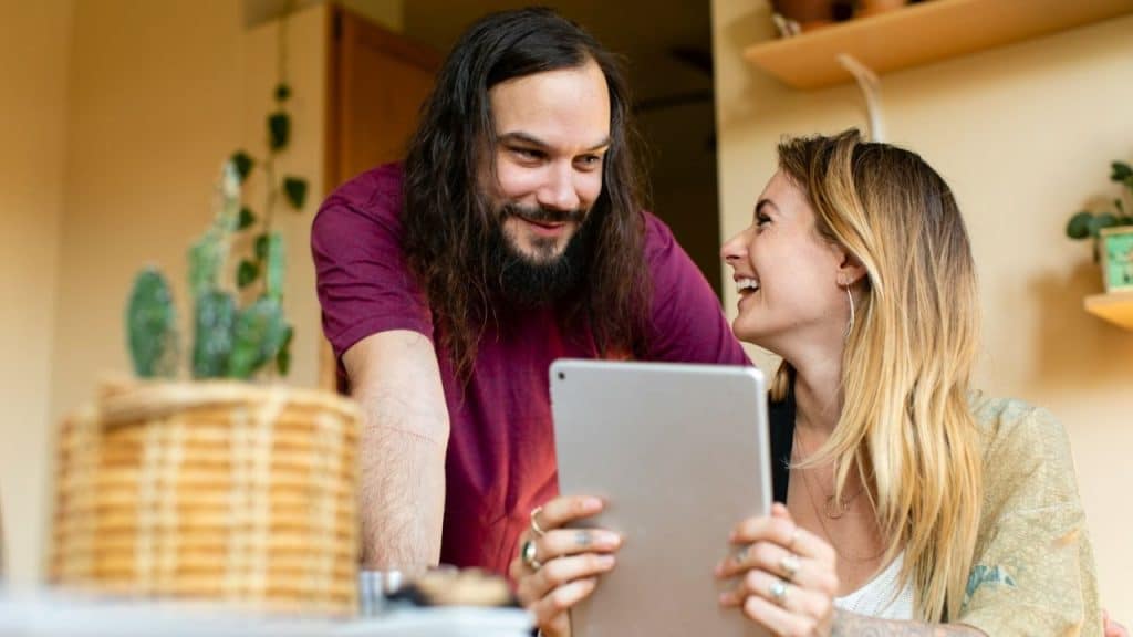 Smiling couple looks at a tablet together; the man has a long beard and hair.