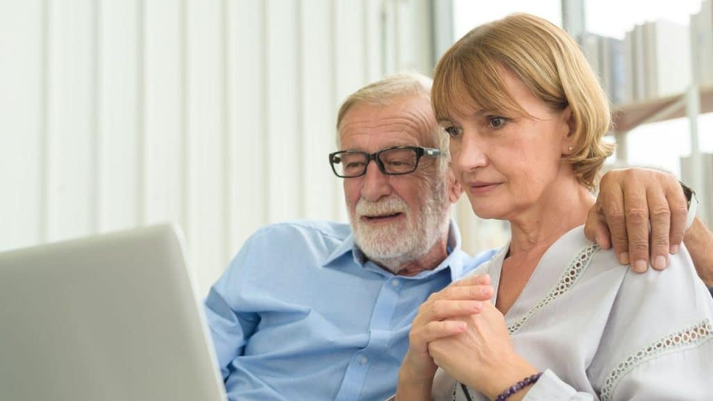 Older couple looking at a laptop screen together, with the man's arm around the woman.