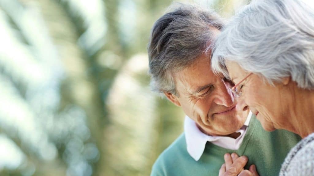 Older man and woman smiling closely together outdoors in a gentle embrace.