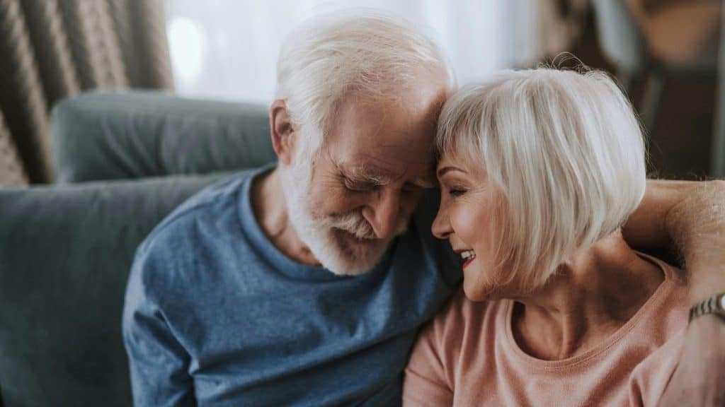 Older couple with white hair embracing affectionately with their foreheads touching.