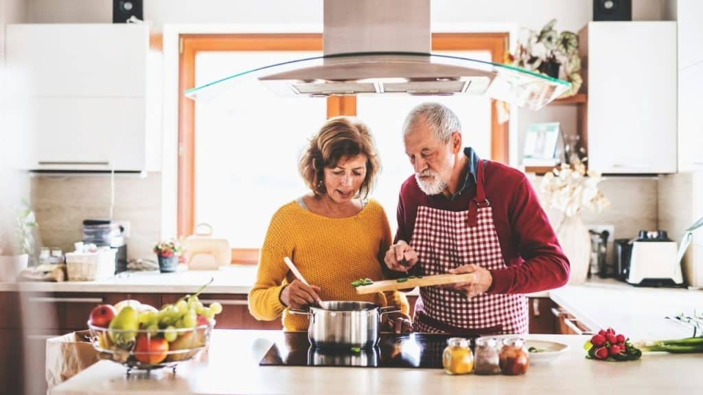 Older couple cooking together in a brightly lit modern kitchen.
