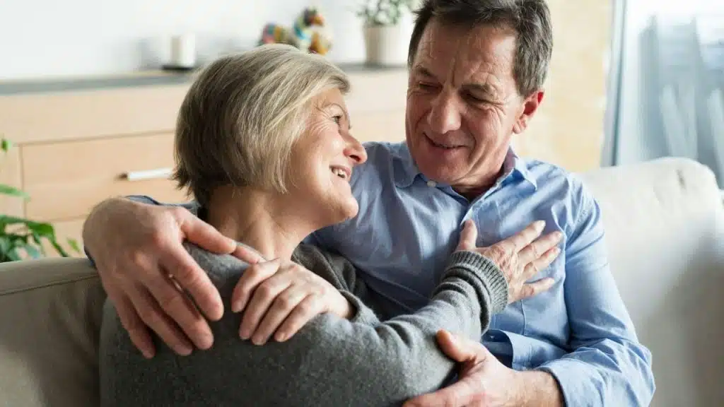 Smiling older couple embracing each other tightly while sitting together on a couch.