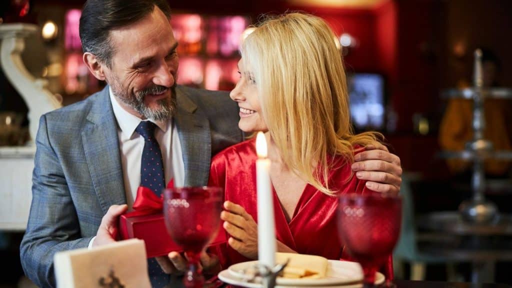 Smiling couple on a romantic date with the man giving the woman a wrapped gift.
